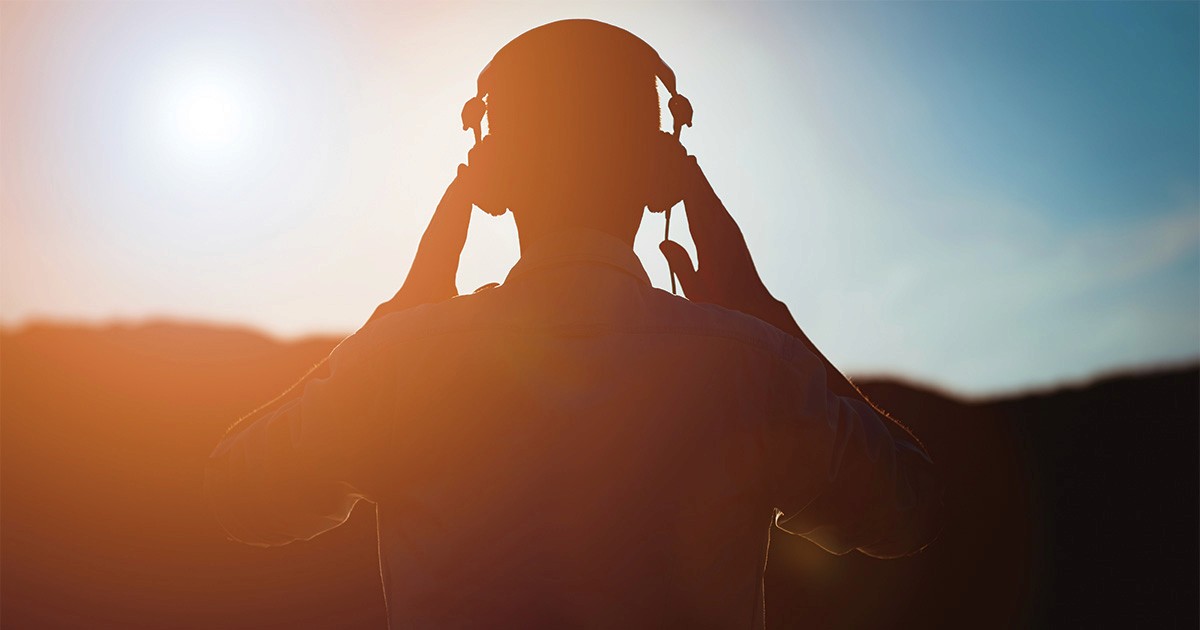 Person listening to music through headphones during a reflective moment outdoors.