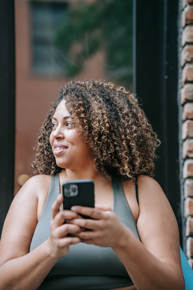 Woman in Sports Clothing Using Her Phone and Smiling