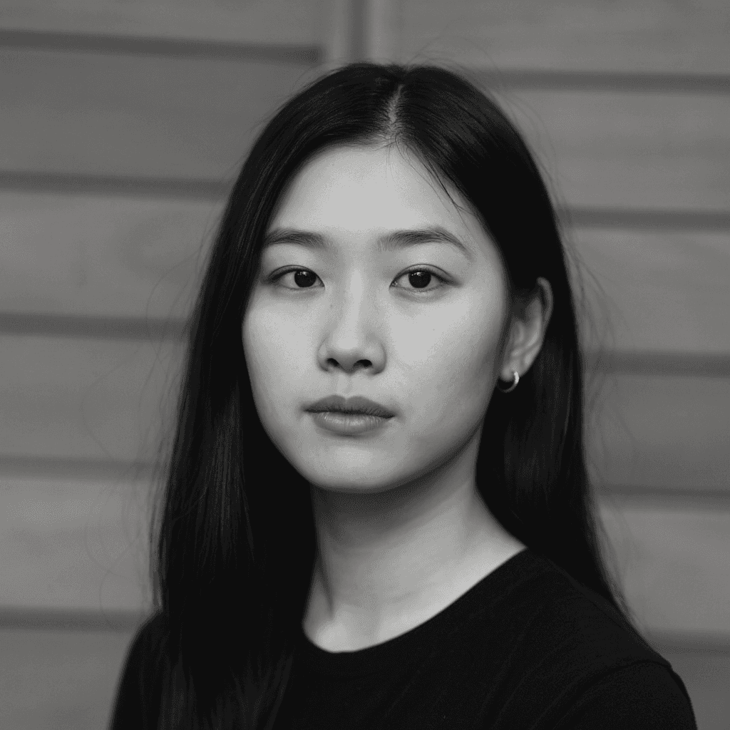 Minimal studio portrait of a confident woman in a white shirt, arms crossed, on a soft gray background.