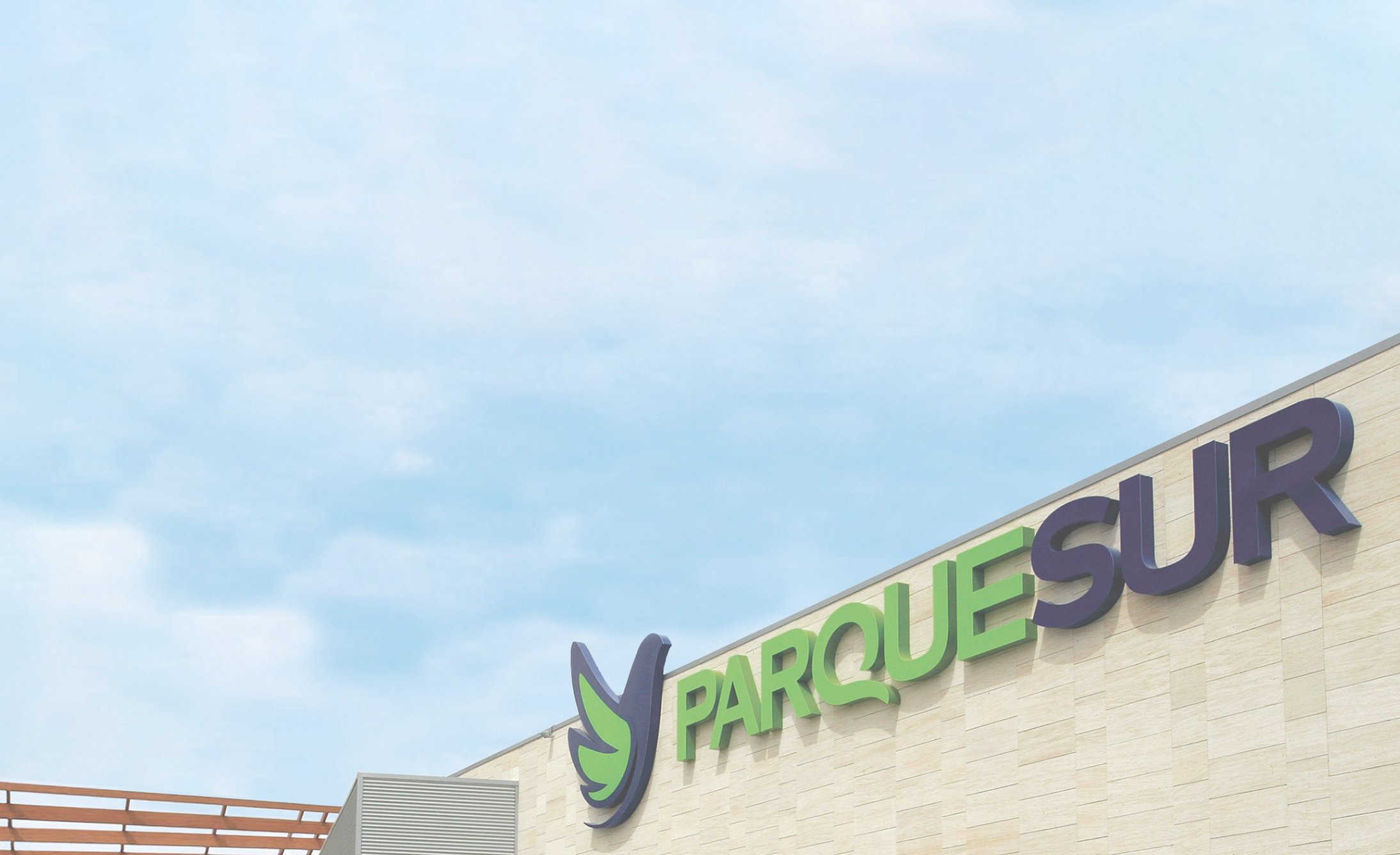 Sign on a building reads "Parque Sur" with a stylized bird logo. The letters are large and bold against a light stone facade, set under a clear blue sky.