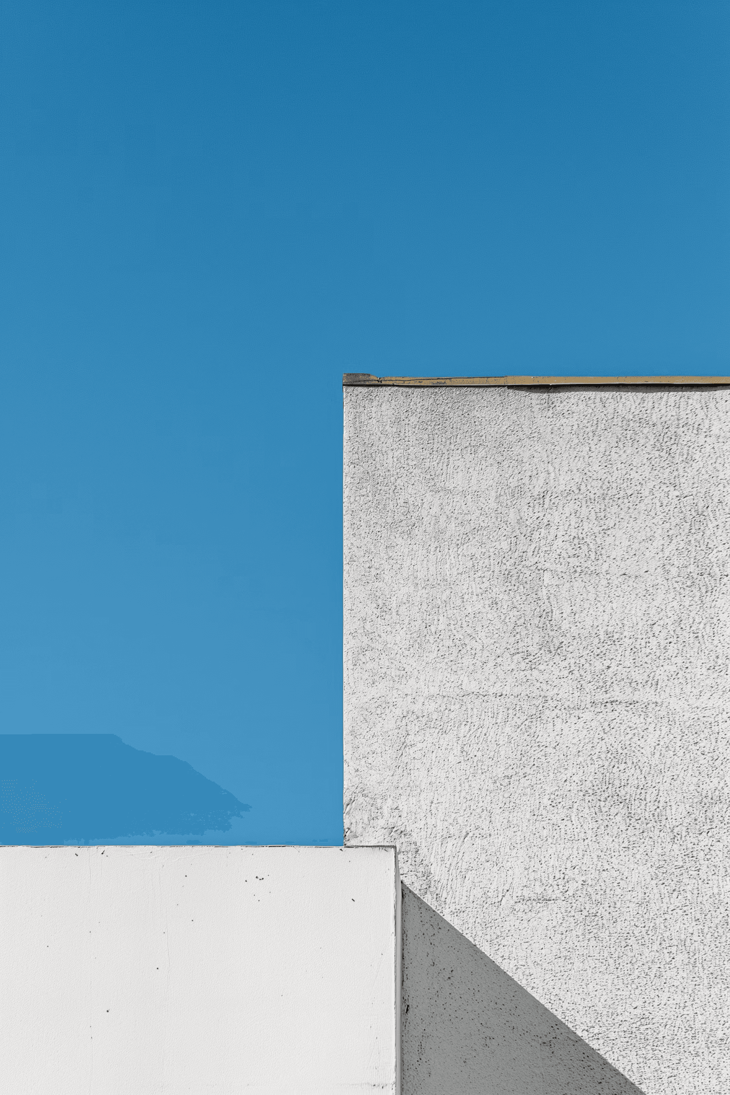 A textured grey wall on the right contrasted with a clear blue sky on the left.