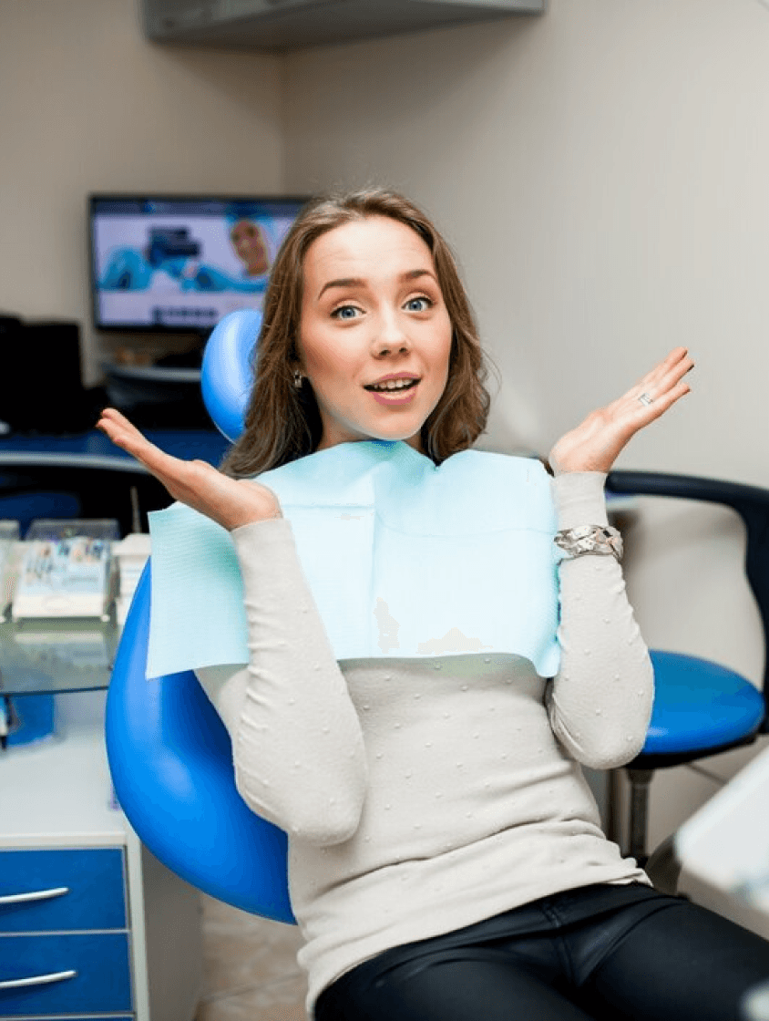  female patient sitting comfortably in a dental chair, smiling and giving a thumbs up, indicating a positive and pain-free experience.