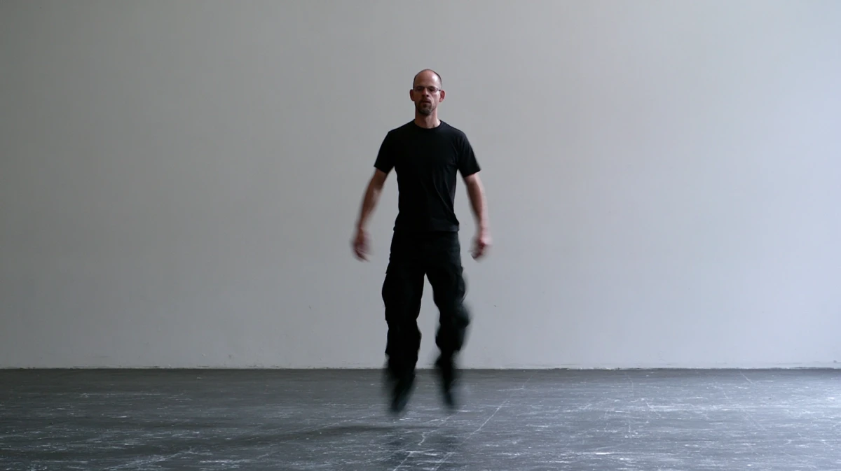 A man standing with soft knees and relaxed, hanging arms, gently shaking his body in an empty room.