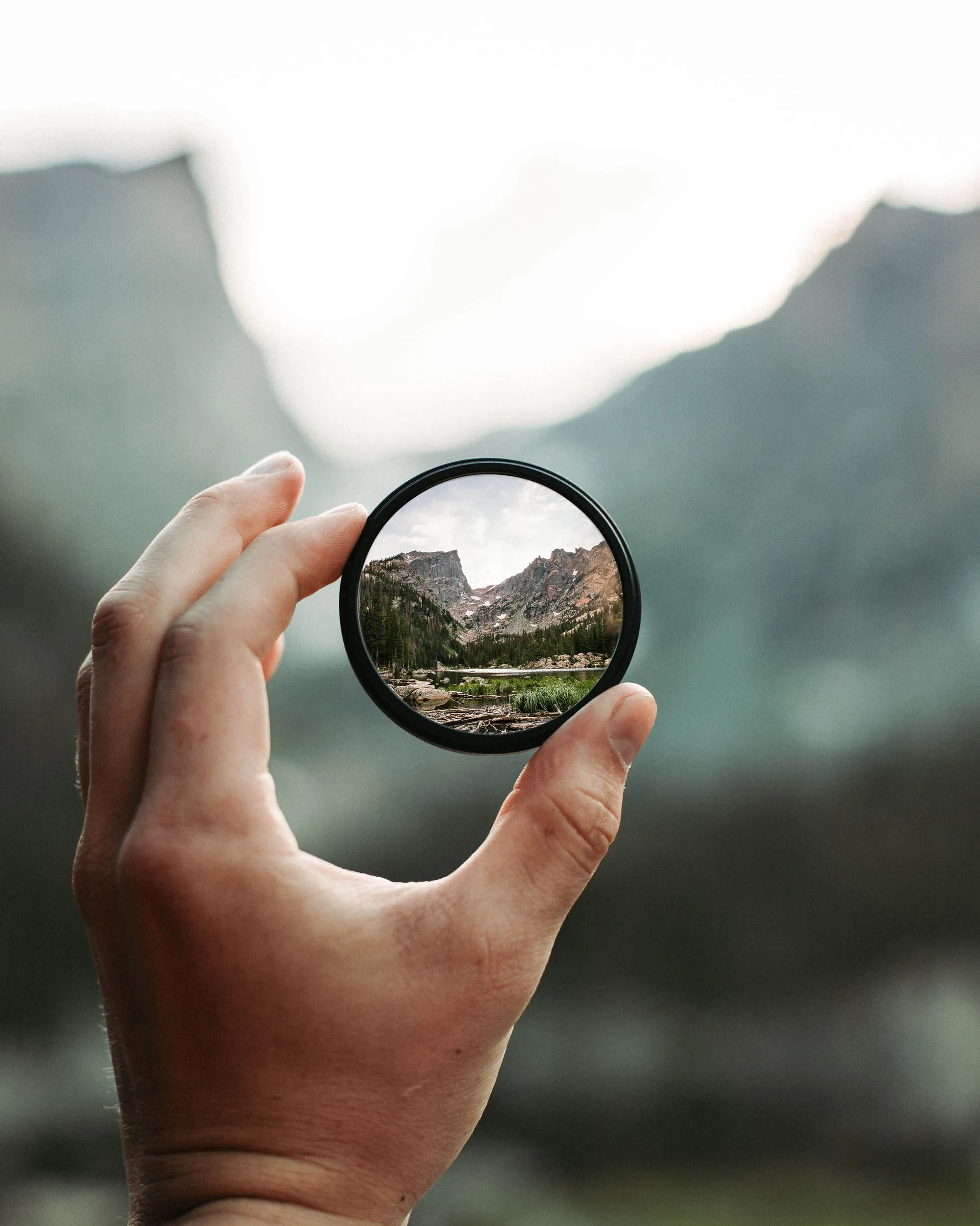Mão segurando uma bola de cristal (lens ball) que traz uma paisagem montanhosa em foco