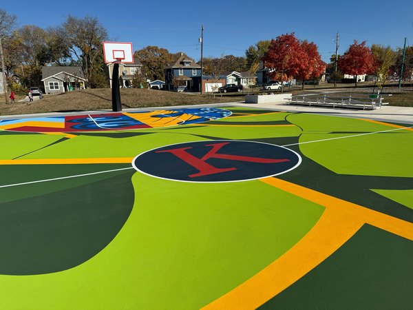 Outdoor basketball court painted in greens and yellow with a red K at center
