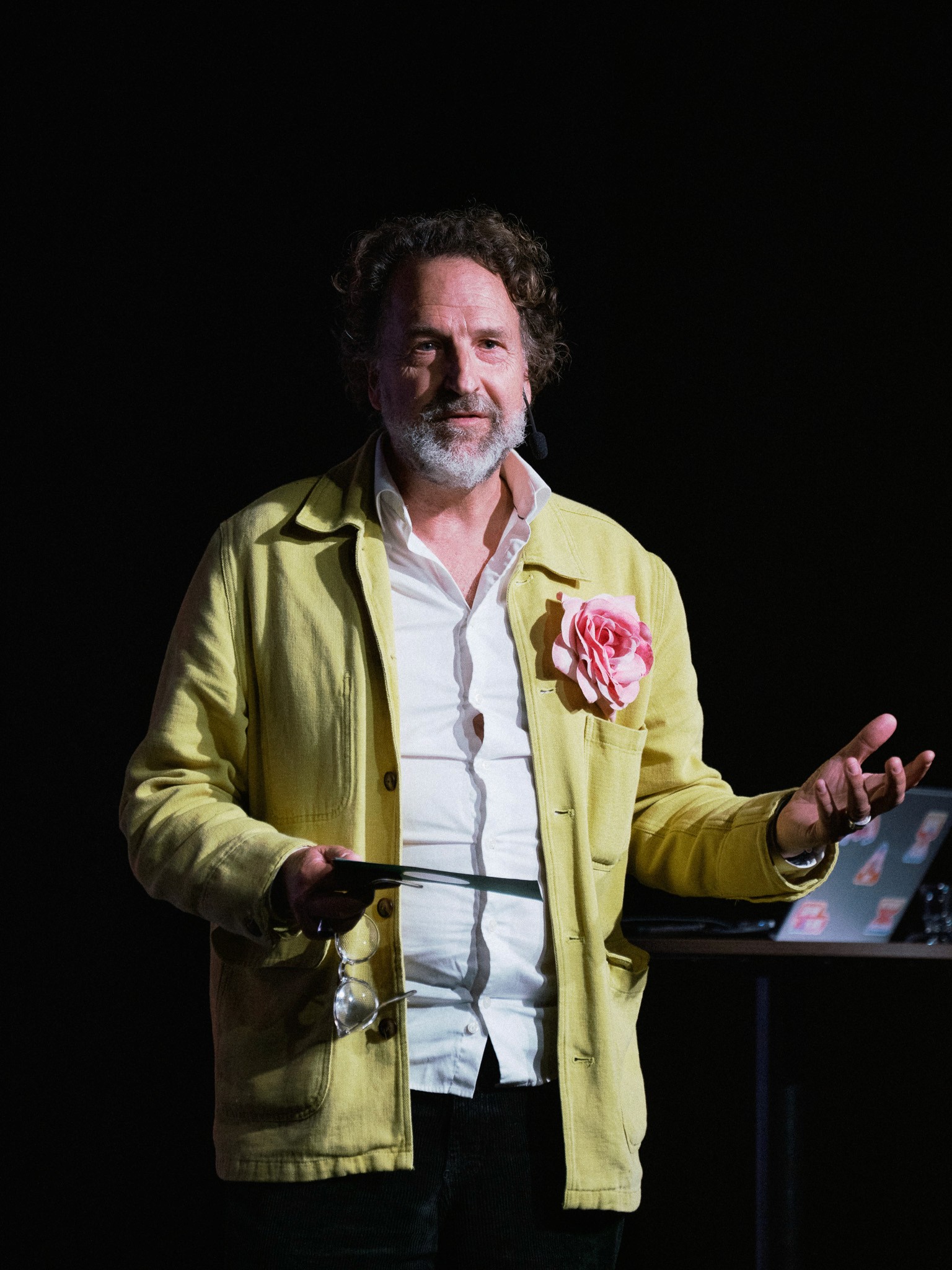 Man i gul jacka med en rosa blomma i bröstfickan talar och gestikulerar