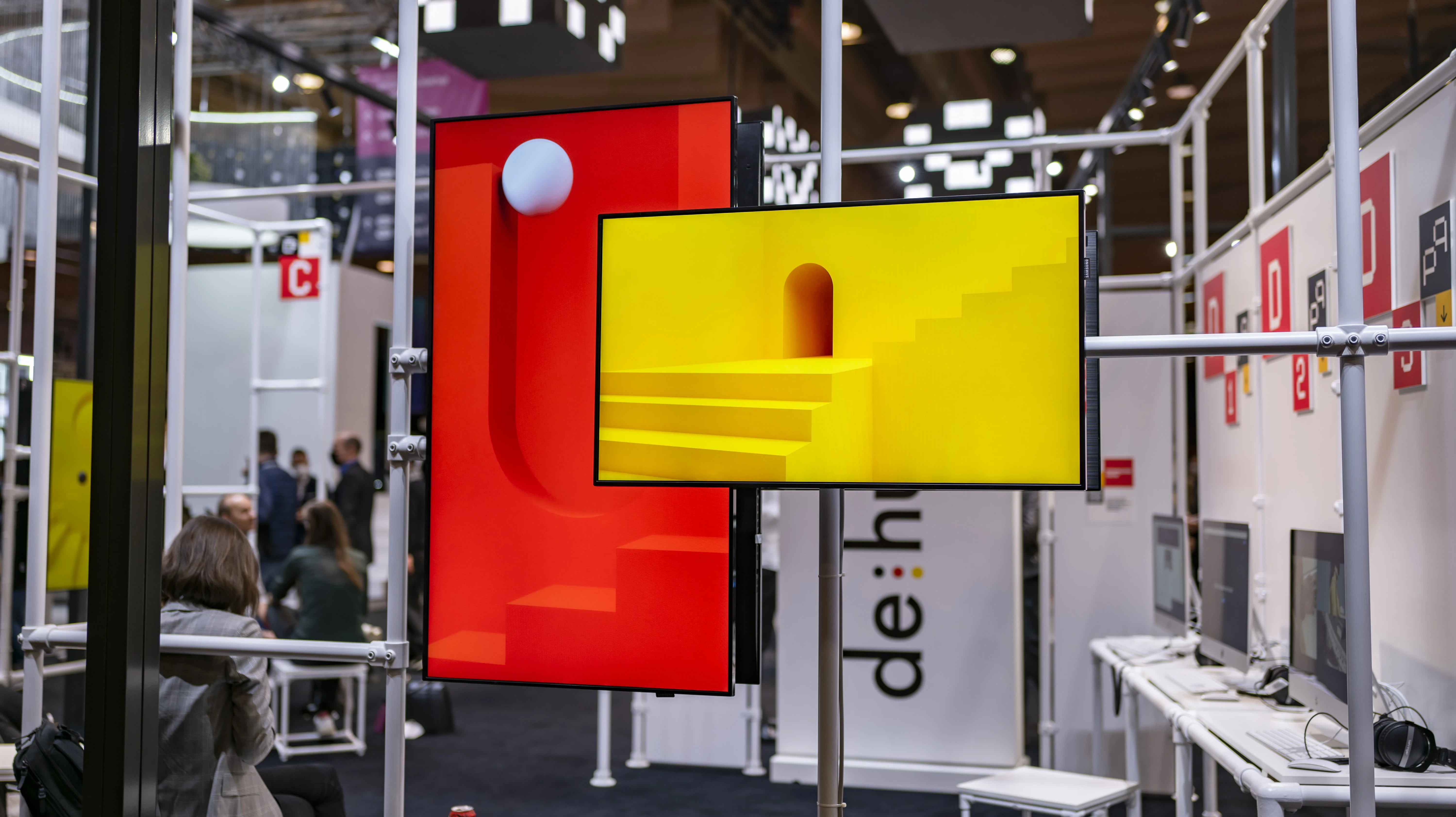 Screens with red and yellow 3D motifs mounted on the white scaffold structure of the German Pavilion at Web Summit.