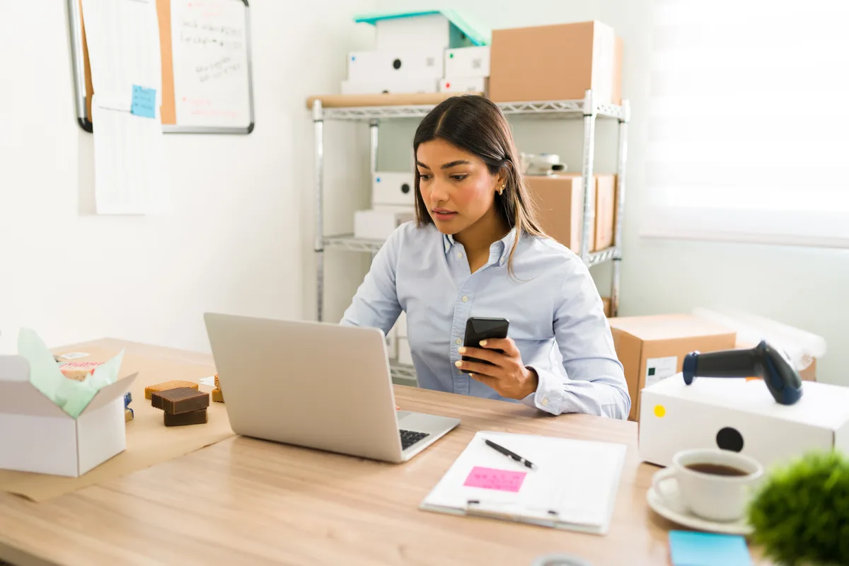 Small business owner checking new customer orders on a laptop and phone