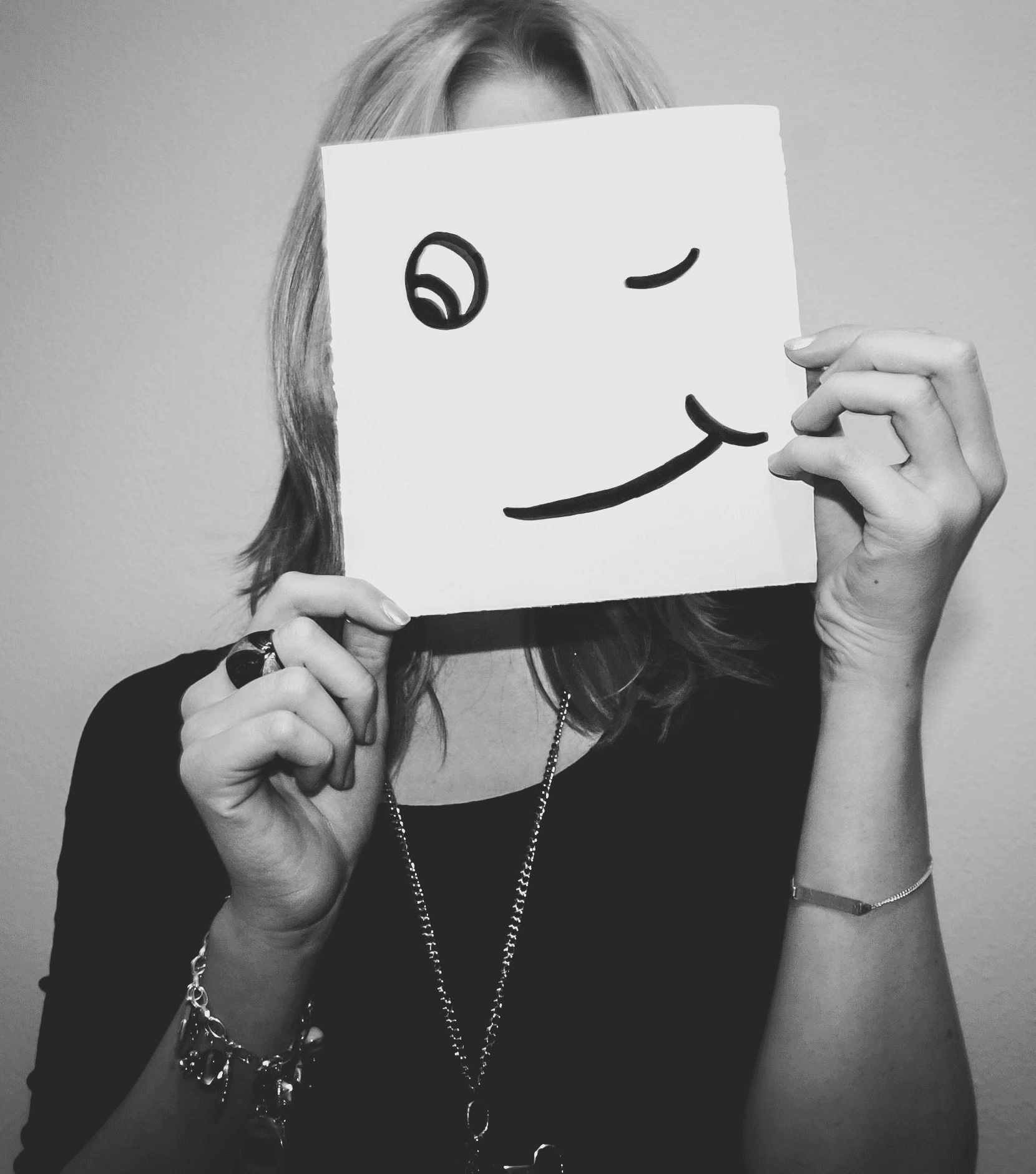 Eine weiblich gelesene Person hält ein Blatt vor das Gesicht auf dem ein großer Smilie gemalt ist.