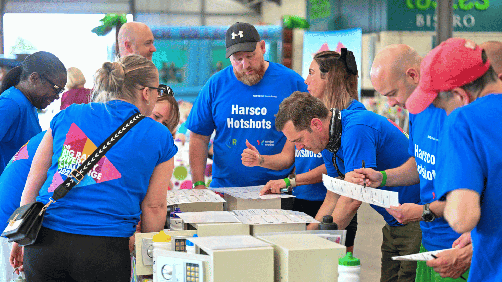 Outdoor team-building event with participants wearing matching blue shirts, taking part in inflatable obstacle courses and games, smiling and cheering, with the words 'ENTER A TEAM' in large bold white and green text across the image.