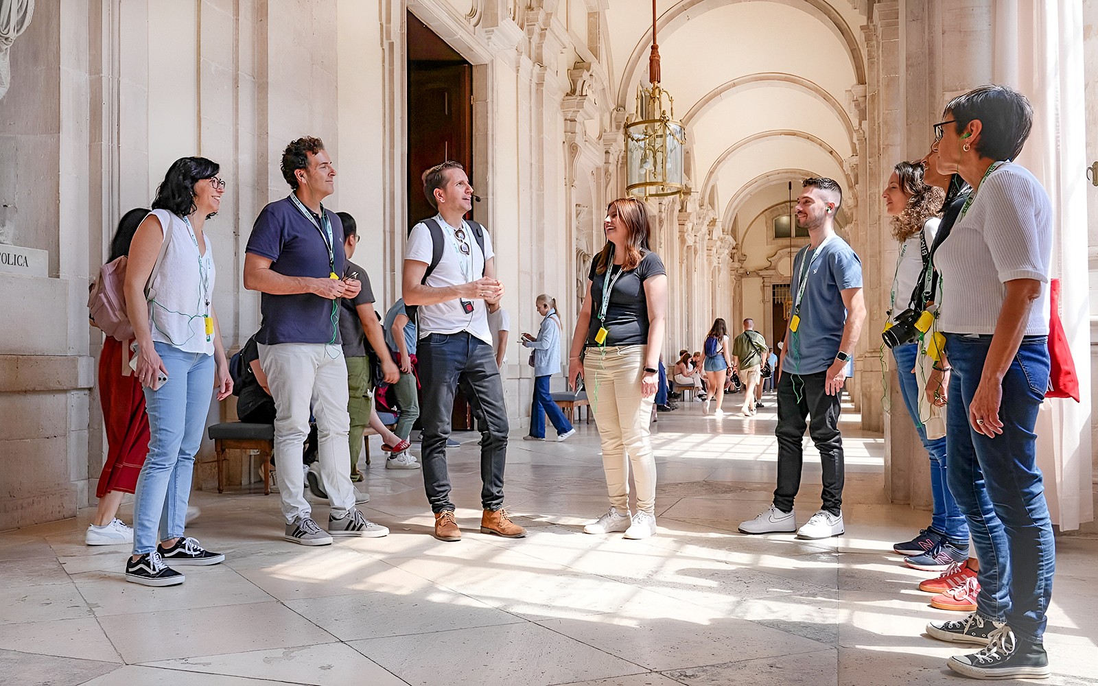 Groep op een begeleide rondleiding in het Prado Museum, Madrid, luisterend naar een gids in een zonnige gang.