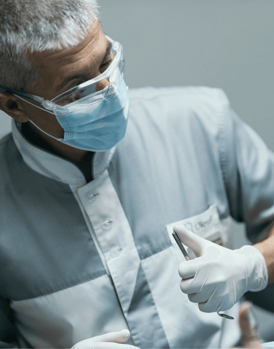 Стоматолог у захисній масці та окулярах схвалює результат лікування, консультує усміхнену пацієнтку, яка сидить у стоматологічному кріслі.