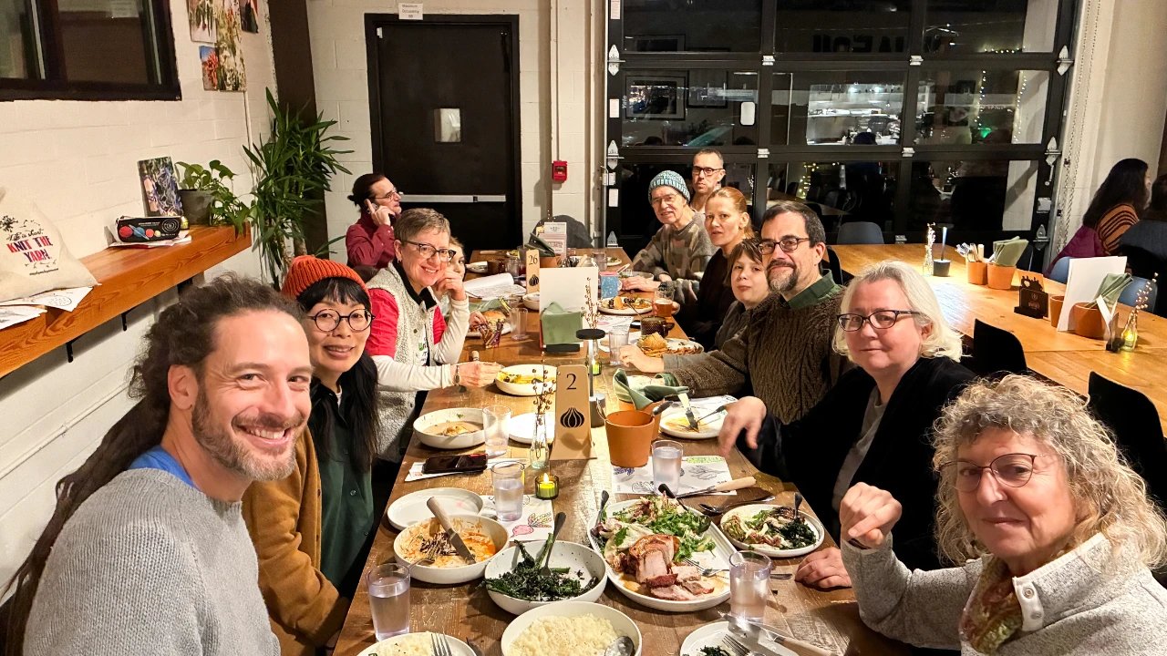 Community members seated together at a long table, sharing a meal and conversation during a group dinner.
