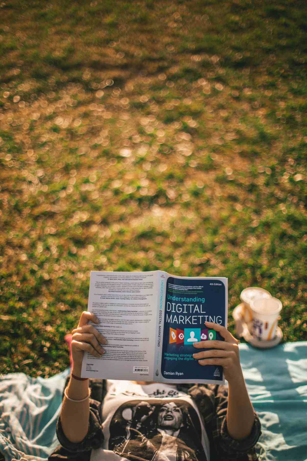 a woman standing on a towel on the grass, reading a book on digital marketing that covers her face