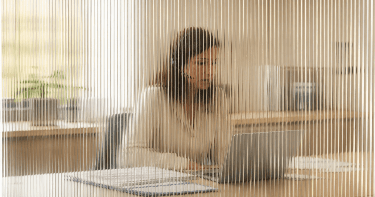 Insurance agent on a headset taking a call at a tidy office desk, seen through vertical fluted glass