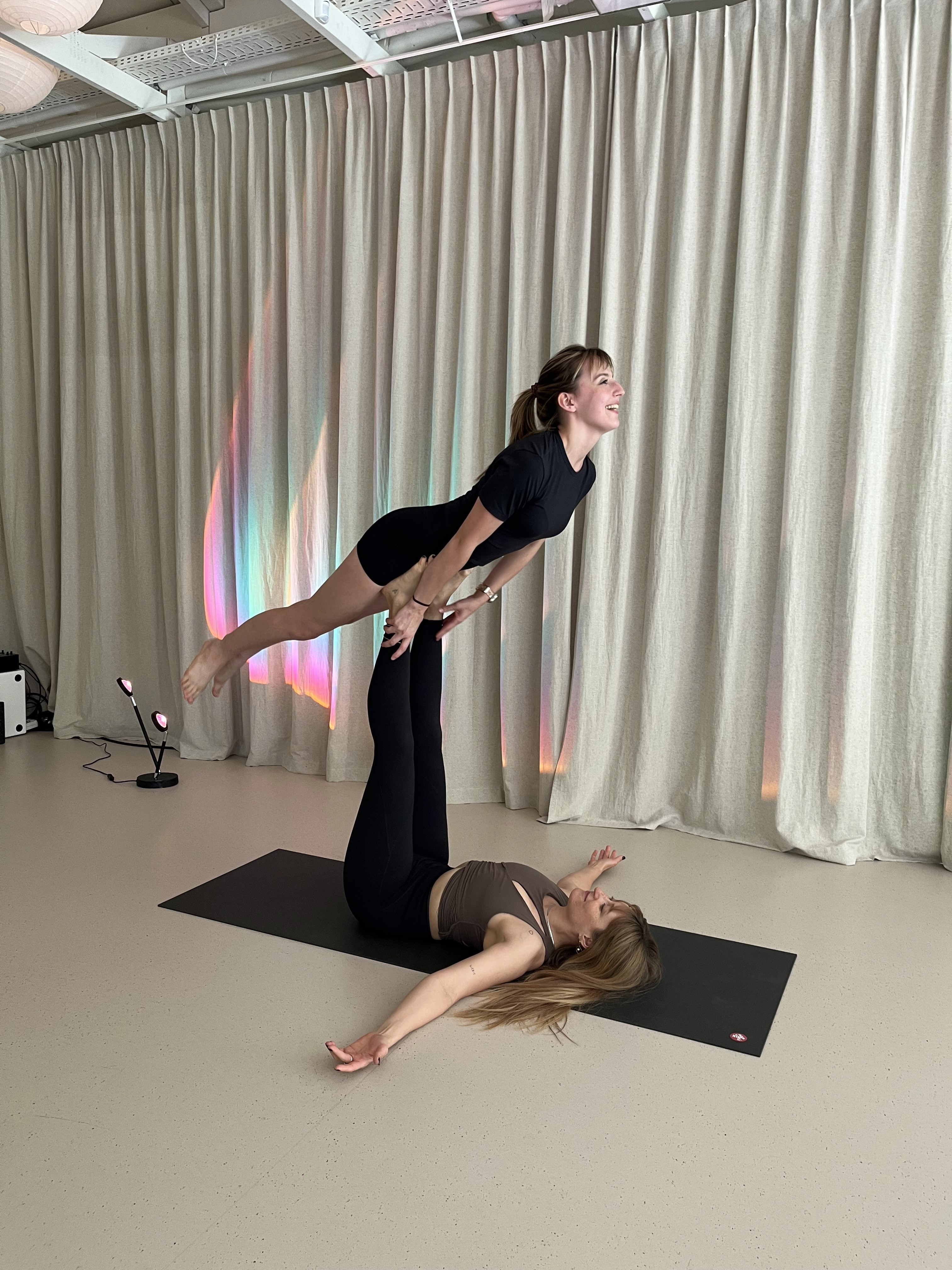 Una persona con una camiseta negra y pantalones de color claro está de pie en la cima rocosa de una montaña al atardecer, sosteniendo una cámara frente a su cara para tomar una foto. Un mar de nubes se extiende detrás de ellos, iluminado por la luz dorada del sol poniente.