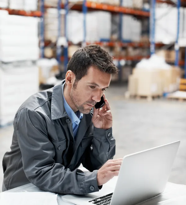 Warehouse dispatcher on a phone call taking an order while checking his laptop