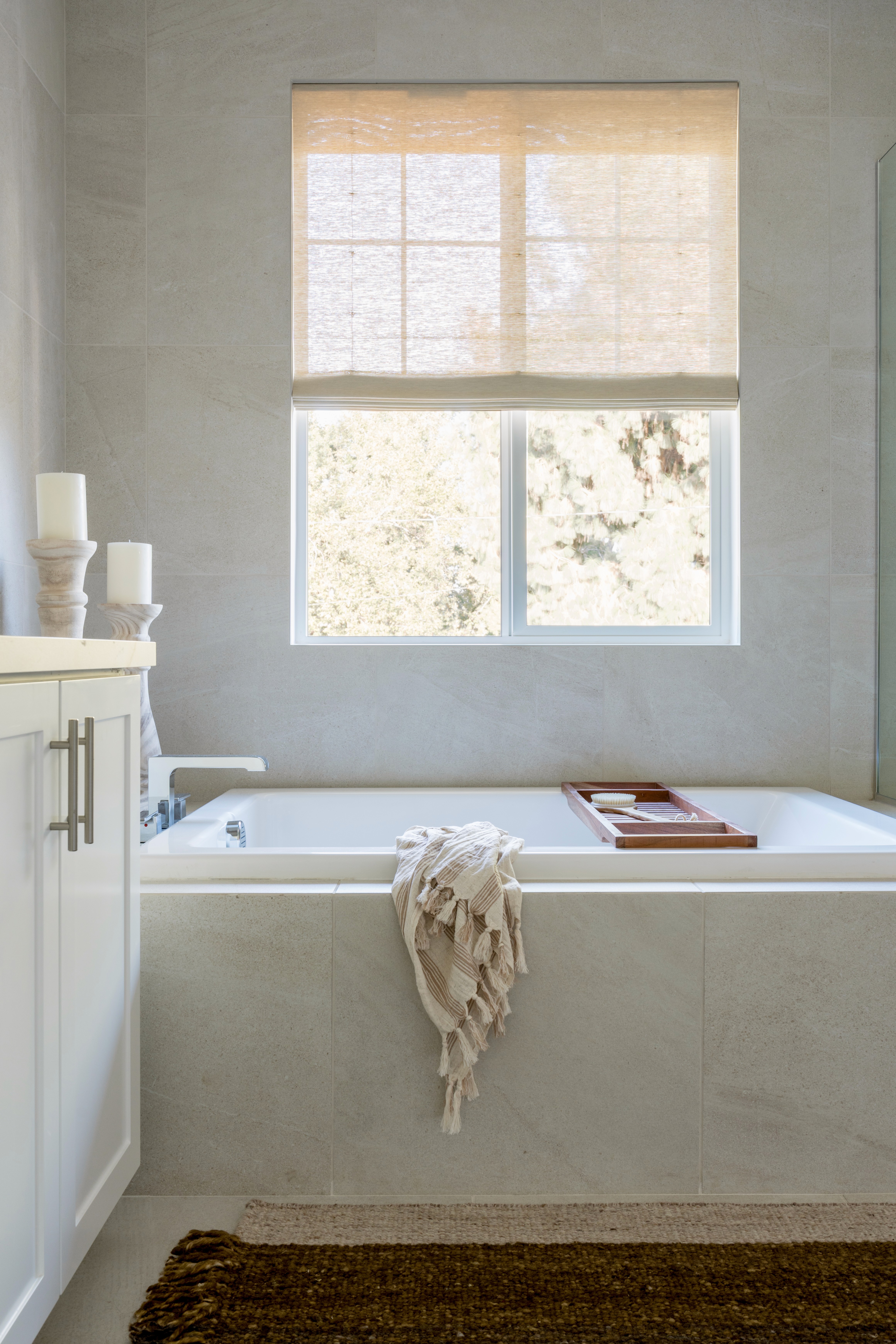 Soft, neutral primary bathroom with rectangular bathtub,  neutral runner, and roman shades by Jubilee Interiors in Arcadia, California