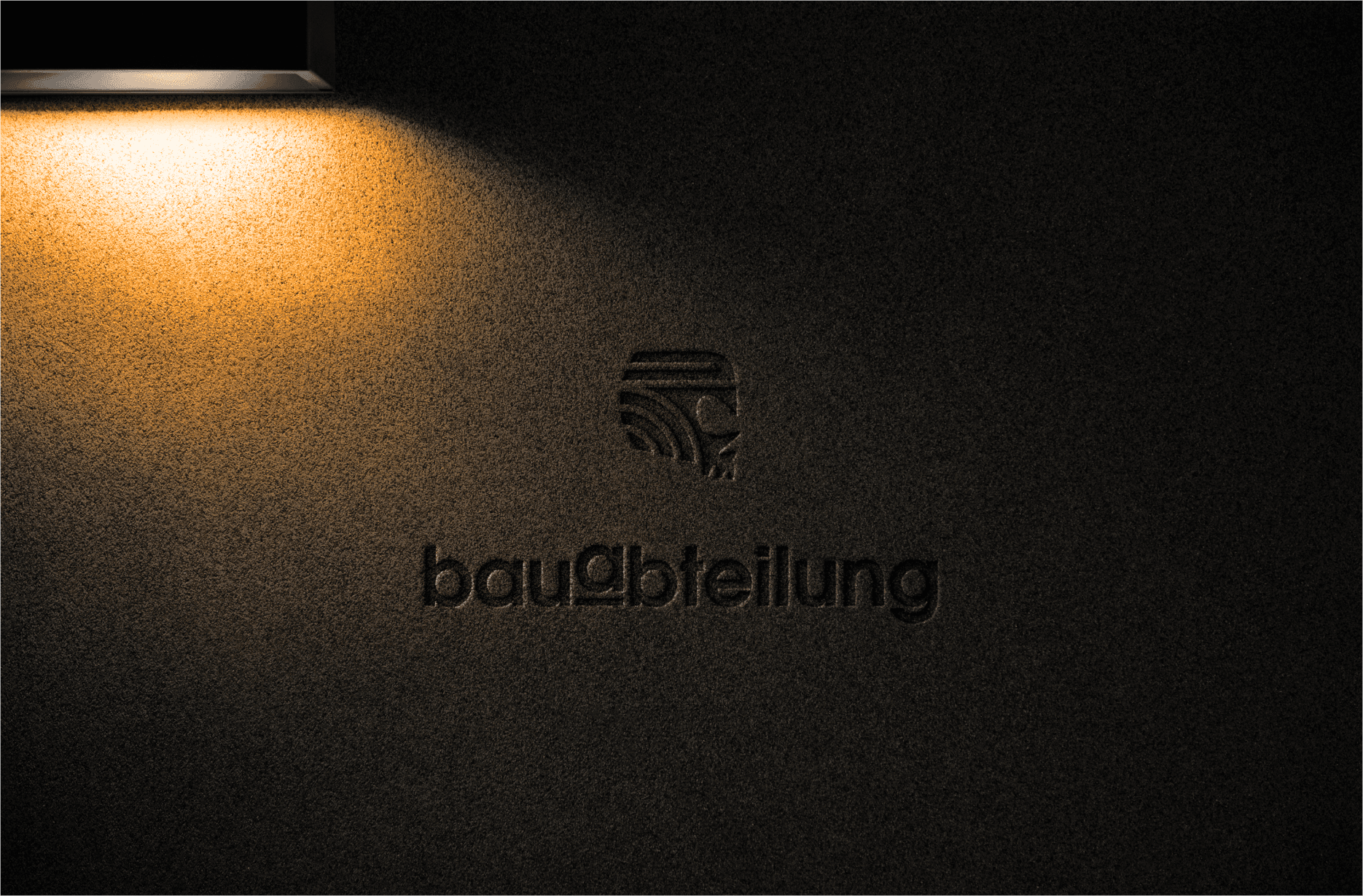 Das Bauabteilungslogo ist in eine dunkle Wand eingeprägt und wird von einem sanften Spotlicht beleuchtet.