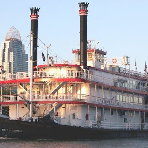 一艘名為「辛辛那提之美女」的河船停靠在一座背景有高樓的城市旁。