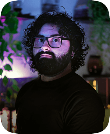 Foto di Claudio Ragusa in uno studio attorniato da luci di vari colori, in un'atmosfera calda e pacifica. Sullo sfondo alcune piante.