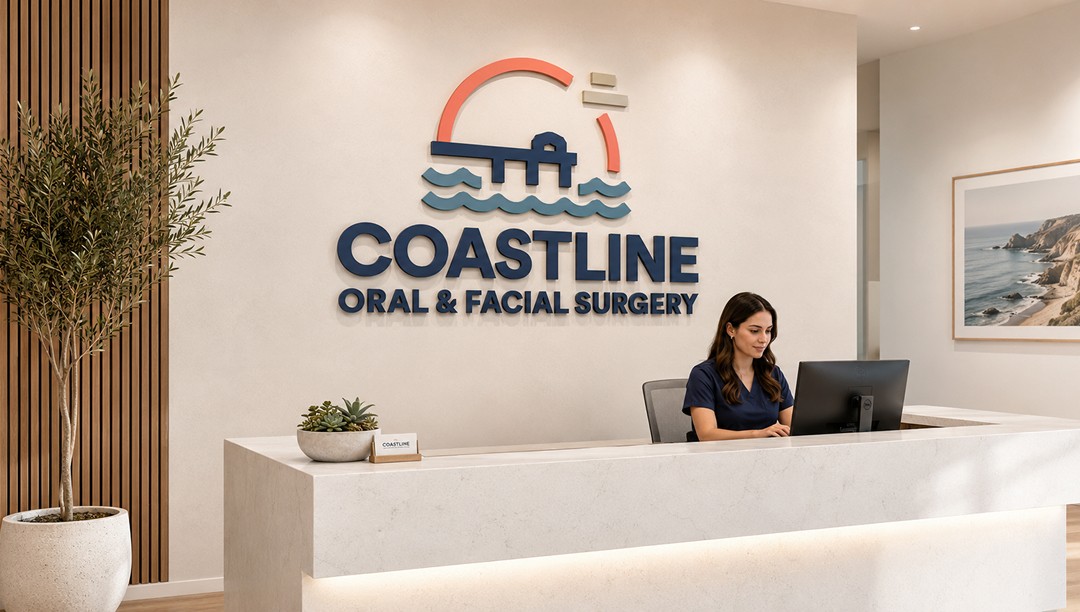 Reception desk with oversized Coastline Oral & Facial Surgery logo mounted on a warm neutral wall behind the receptionist.