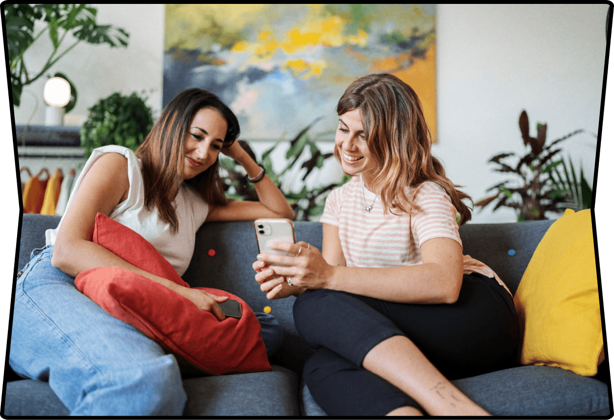 two women looking at one smartphone while smiling.