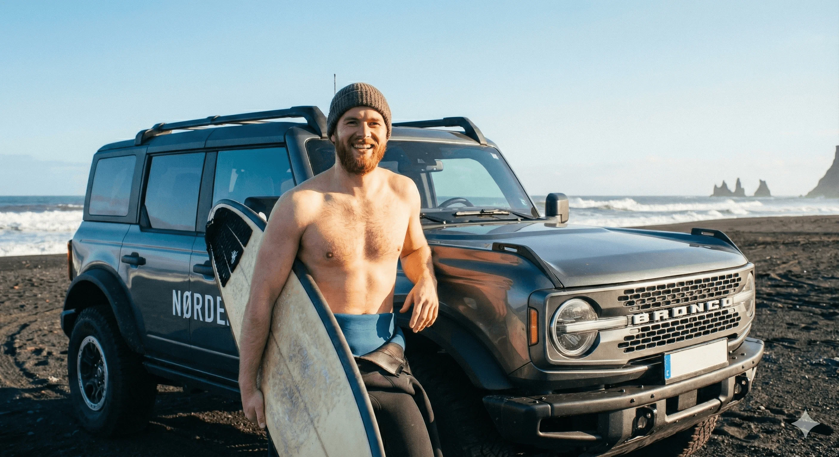 Shirtless surfer holding a board next to a jeep.