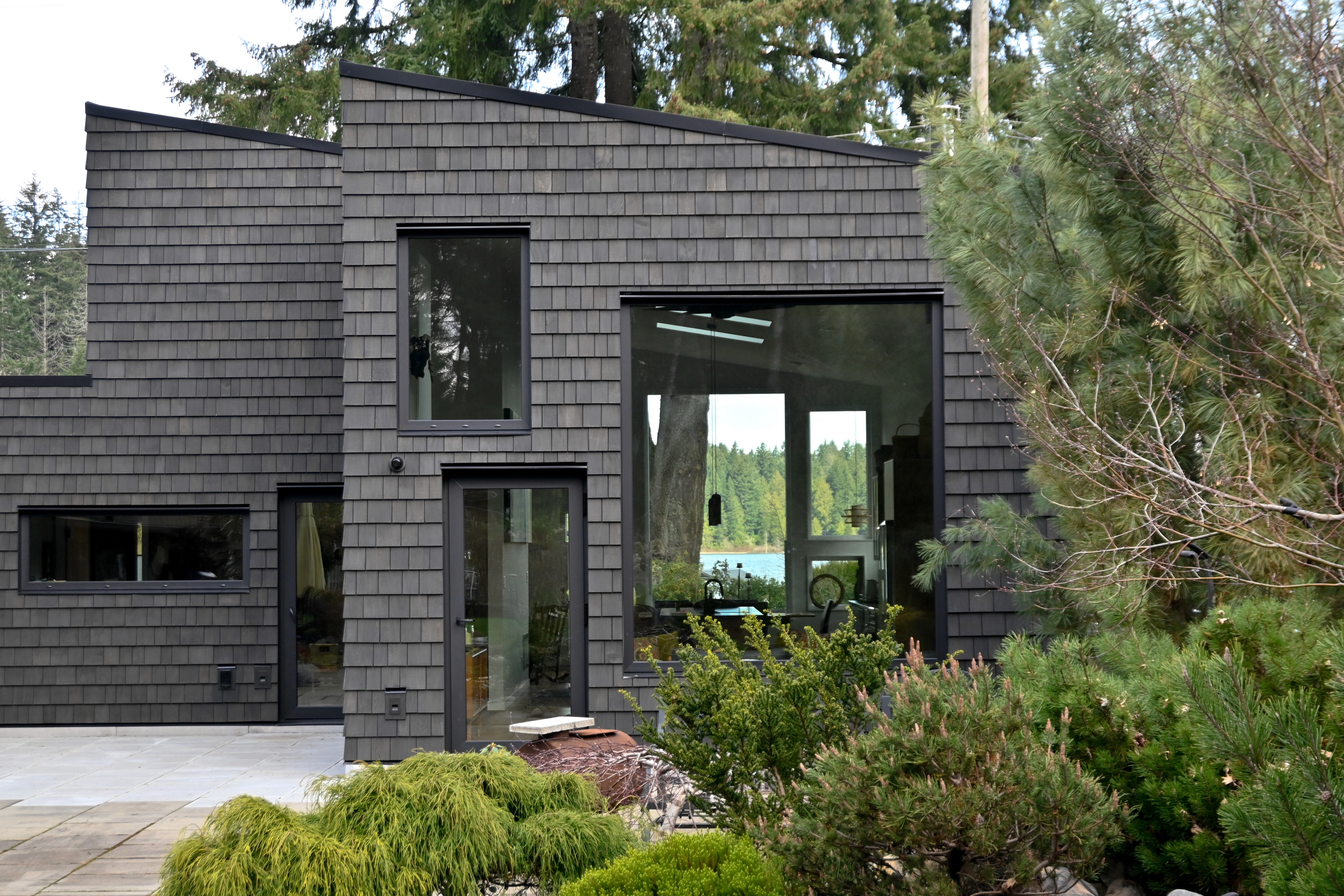 A serene outdoor seating area with two chairs, surrounded by lush greenery and a glassed-in structure.