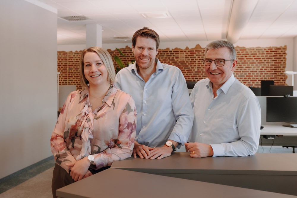 Die drei Geschäftsführer der Geschäftsführung von SLB stehen nebeneinander an einem Tresen in einem modernen Büro.