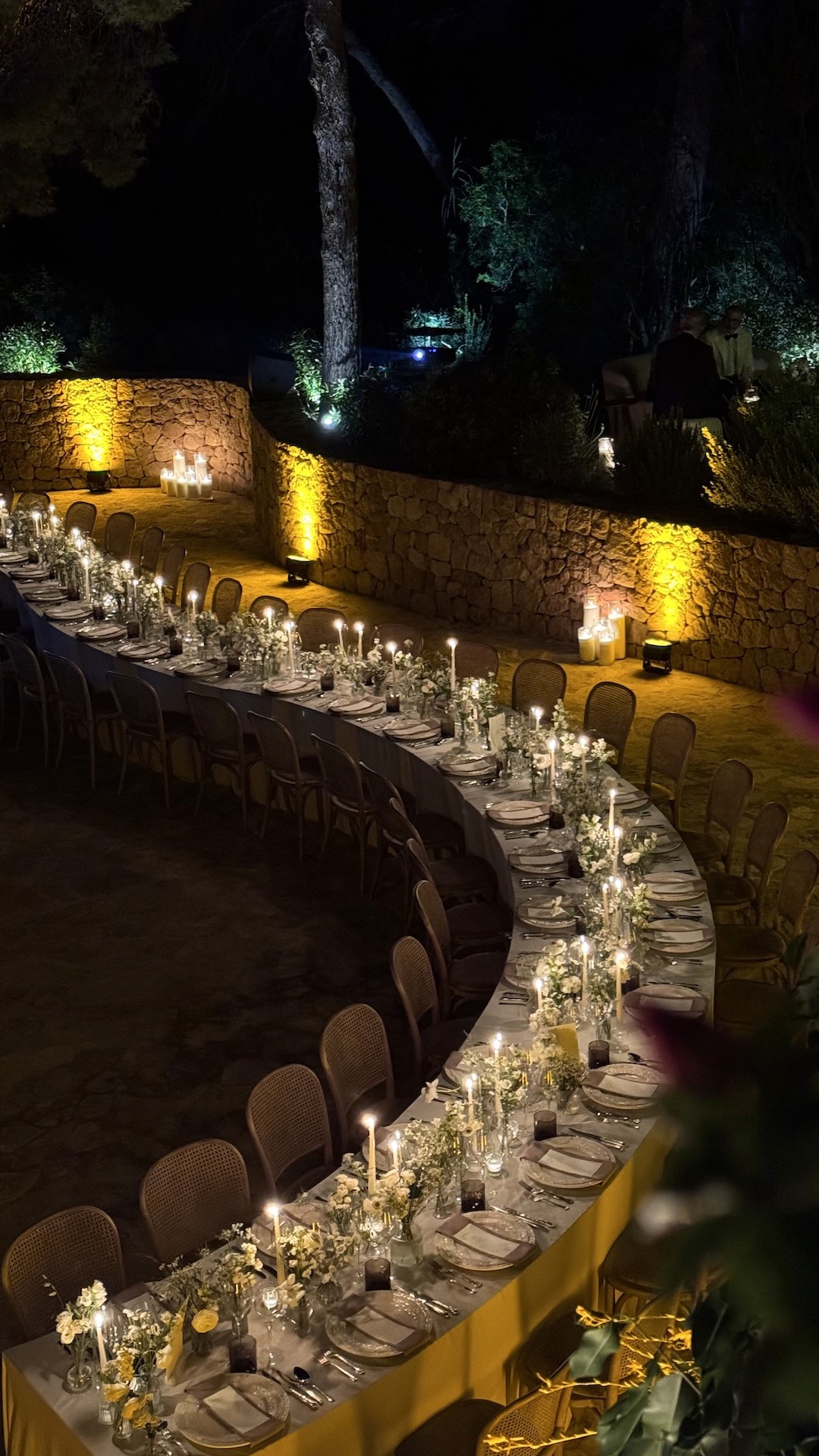 Curved candlelit dinner setup surrounded by stone walls at nighttime Ibiza wedding.