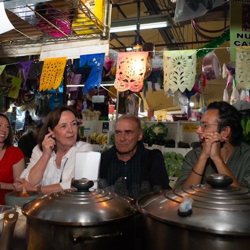 Mga manlalakbay na nakaupo sa isang tradisyonal na tindahan ng pagkaing Mexicano, napapalibutan ng makukulay na dekorasyon.