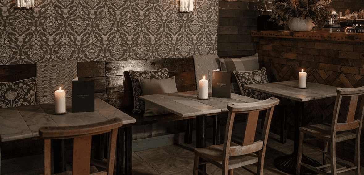 White plate with roasted chicken served in a golden sauce with herbs and capers, placed on a terrazzo tabletop in sunlight.