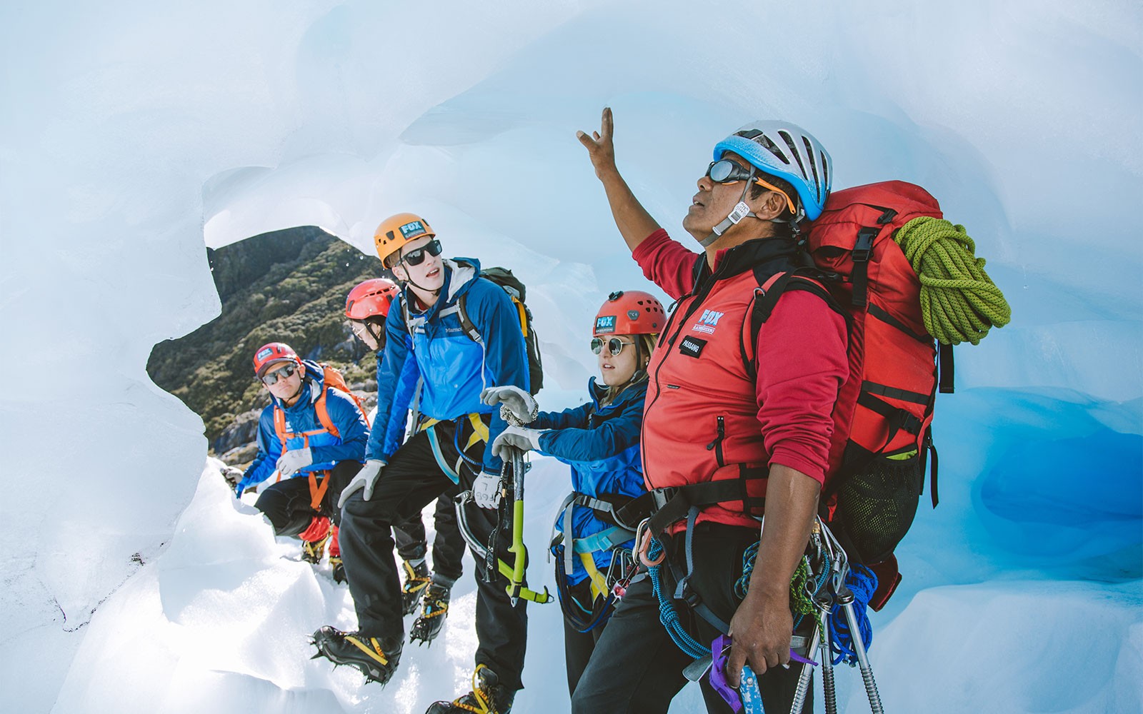 Guía liderando un grupo de turistas en una caminata en helicóptero por el glaciar Fox, señalando formaciones de hielo.