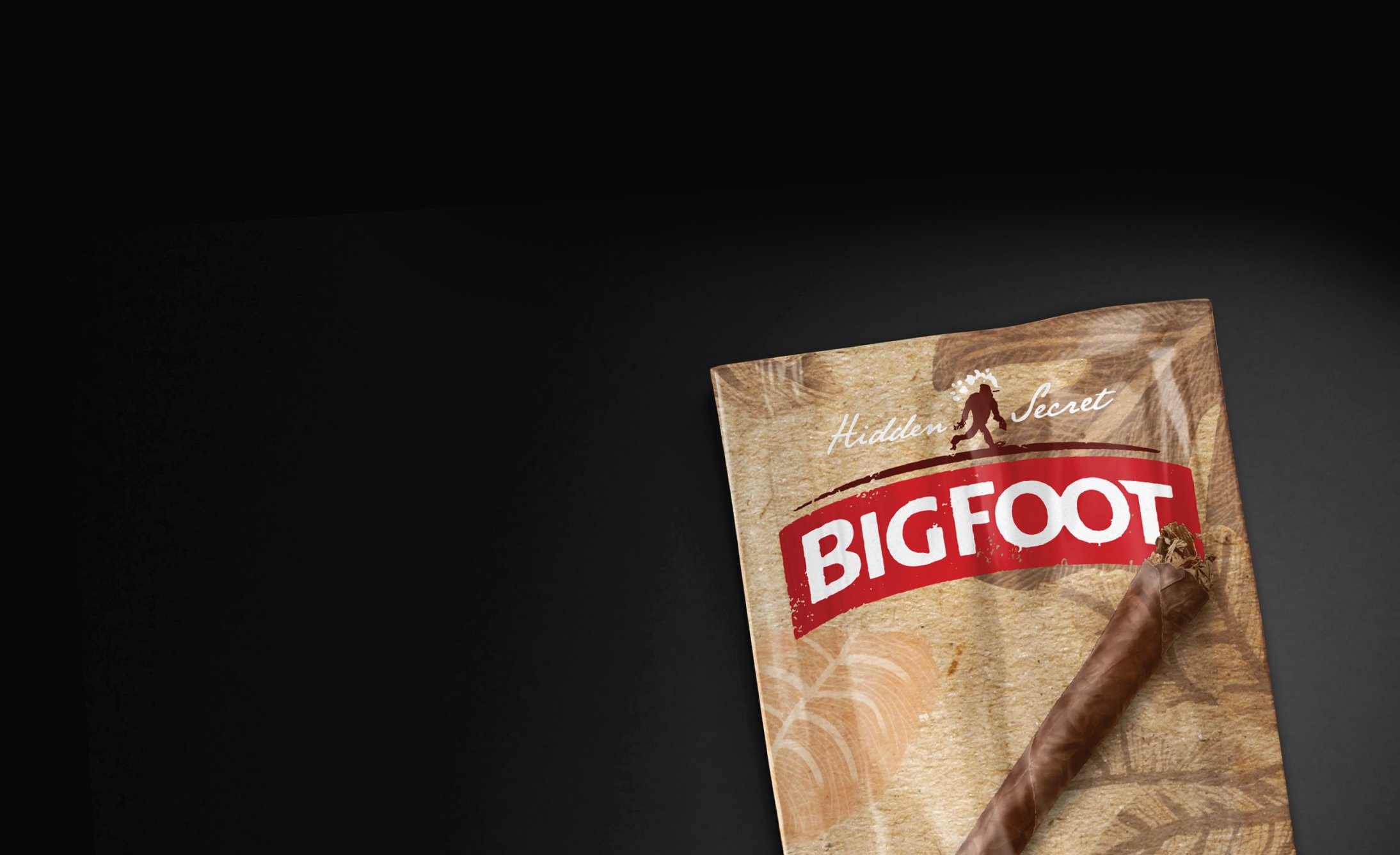 A partially visible cigar rests on a brown package labeled "BIGFOOT" in bold red. The design includes subtle leaf patterns, conveying a sense of mystery.