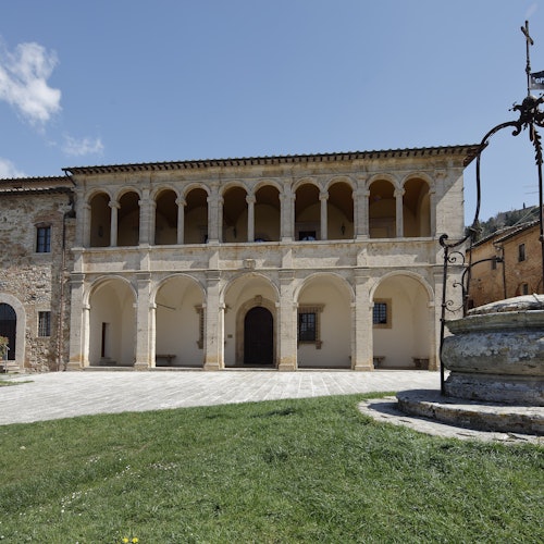 具有拱形柱廊的歷史建築，前景是一口井，和一個在晴朗藍天下的草坪courtyard。