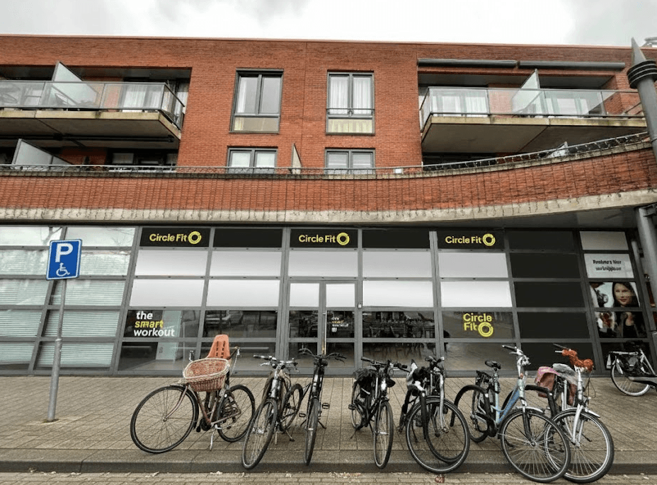 A Circle Fit with large windows featuring yellow signs and an entrance door, with customers visible inside.