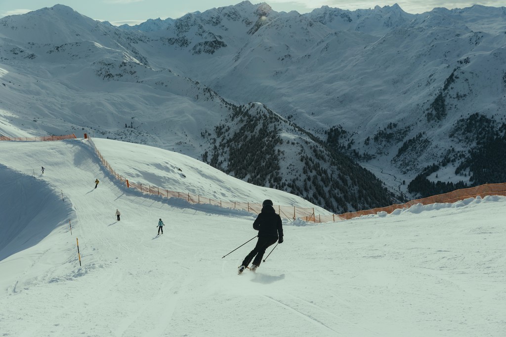 Skiers descending snowy mountain slope with scenic alpine backdrop.
