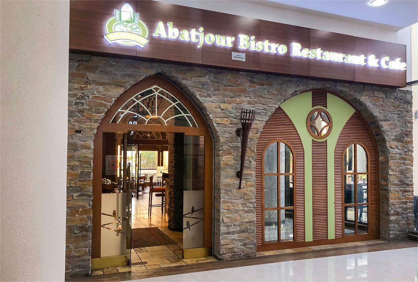Rustic stone facade of Abatjour Bistro in Remraam Dubai with arched doors and inviting cafe interior.