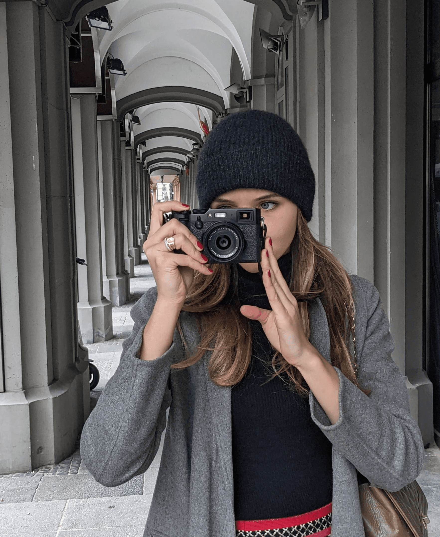 I am photographing under a stone arcade, wearing a beanie, and grey coat.