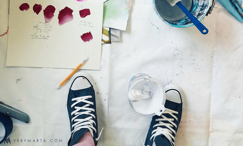 A pair of Chuck Taylor sneakers standing on a floor covered with paper and paints