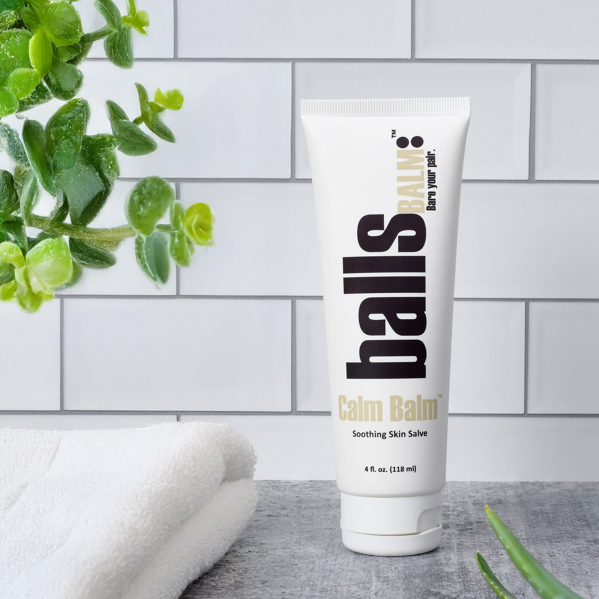 lifestyle product photo of men’s balm tube on white tile with towel and plant