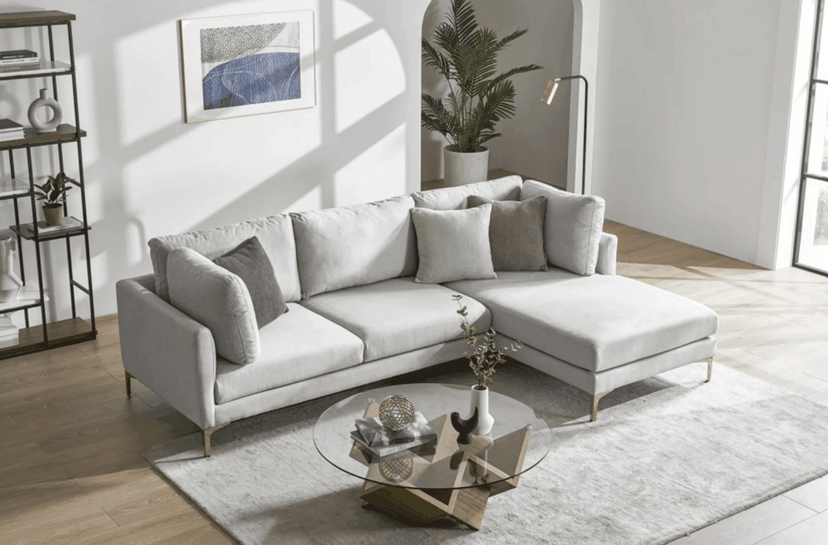 Light gray Castlery Adams chaise sectional sofa in a bright living room with modern decor & a round glass coffee table.