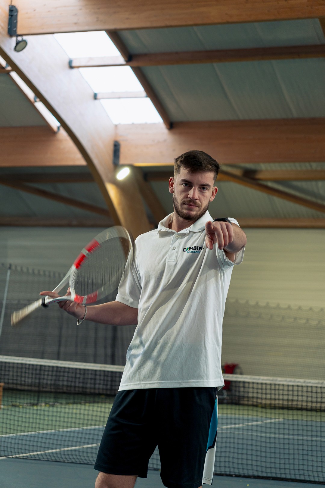 Aurélien Arlot pointant du doigt, raquette en main, sur un court de tennis couvert.