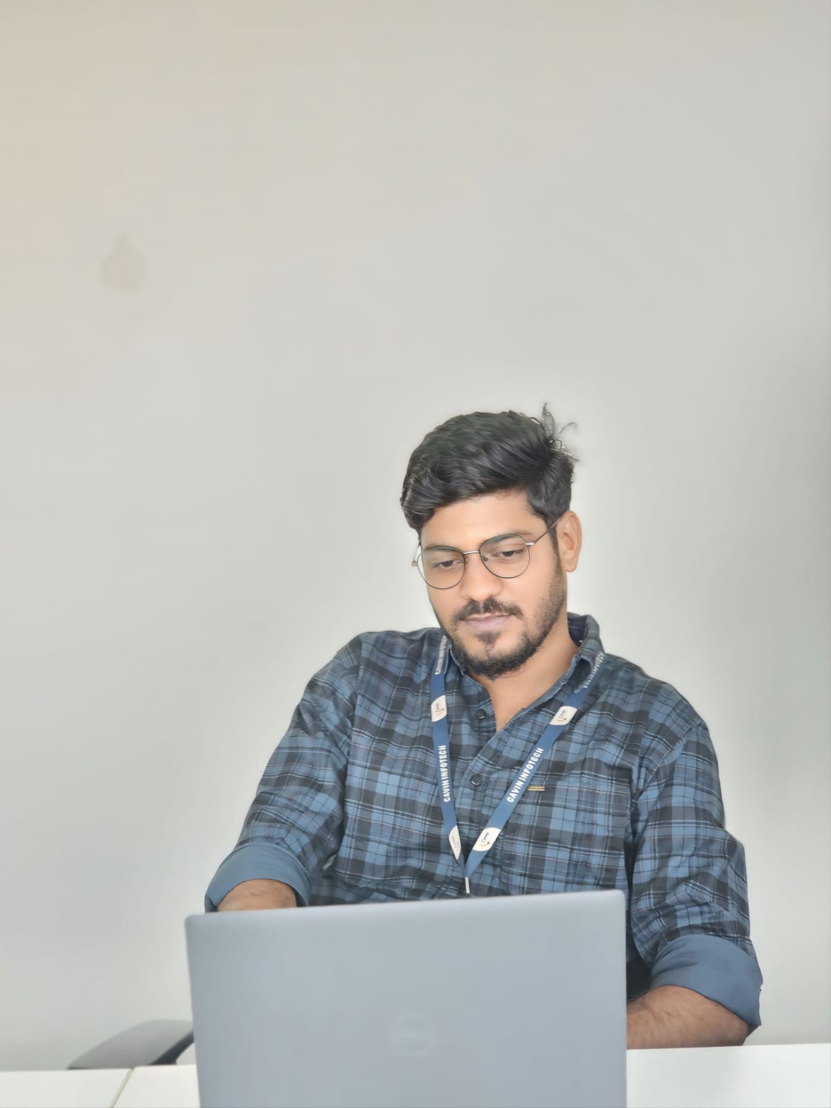Overhead view of a man sitting on the floor beside a desk, smiling while holding a smartphone, with a laptop and notebook placed on the table above him.