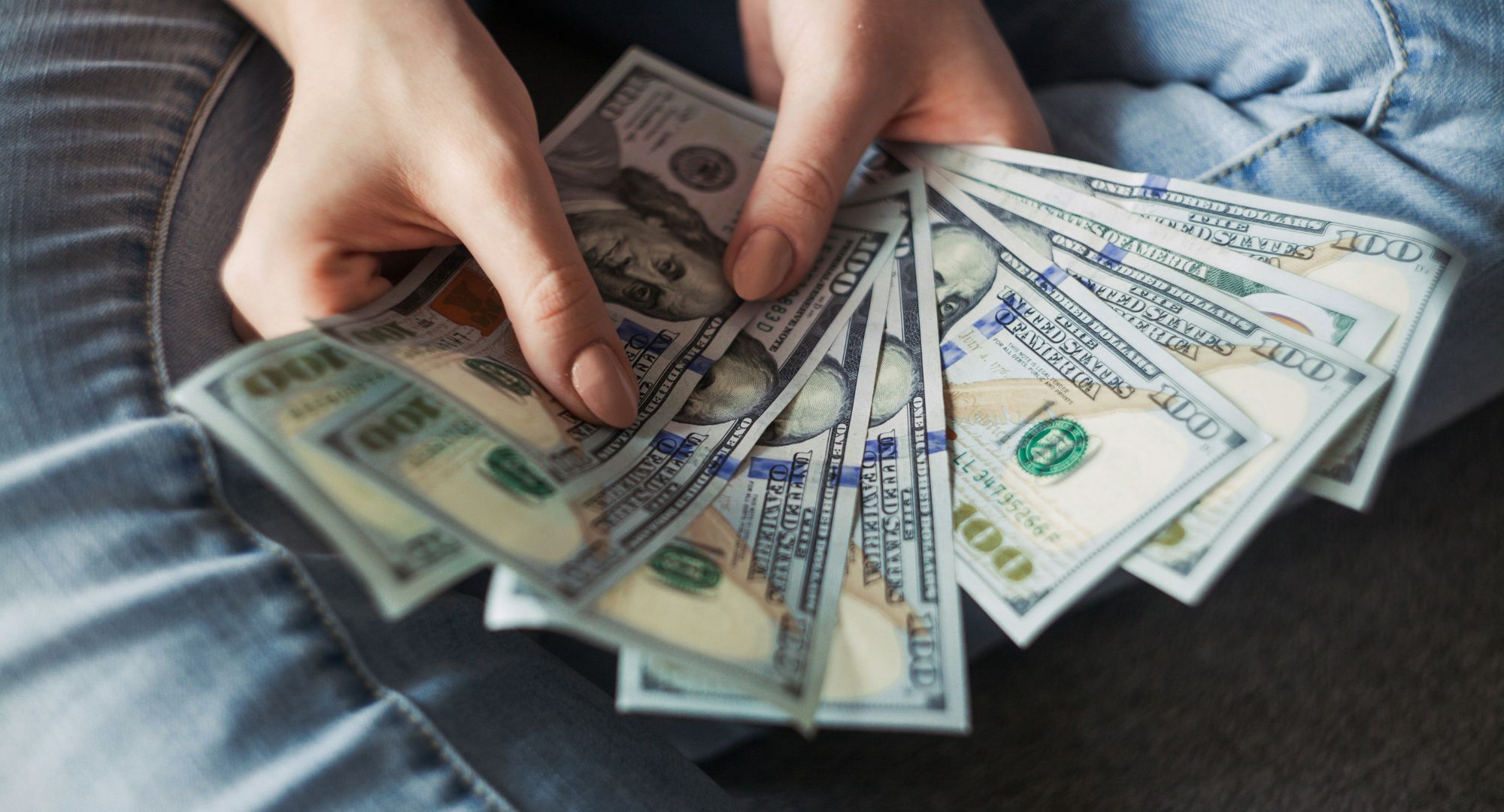 pessoa segurando com as duas mãos um leque de notas de dólares