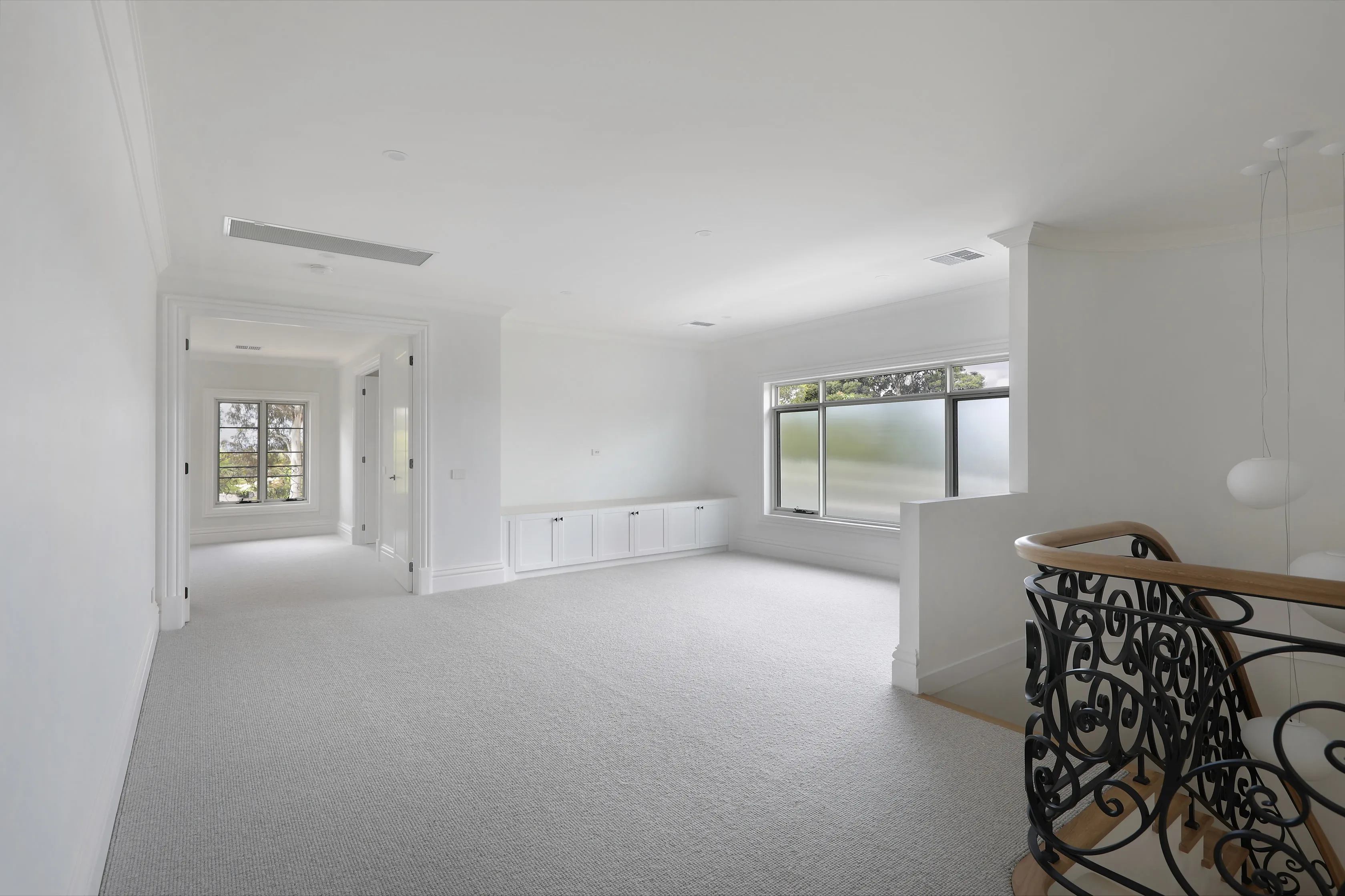 Carpeted upstairs retreat with white walls, ornate cornices, built-in cabinetry, a frosted picture window and the curved iron-and-oak balustrade of the staircase