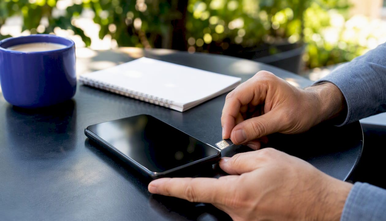 Hands inserting SIM card into smartphone on desk