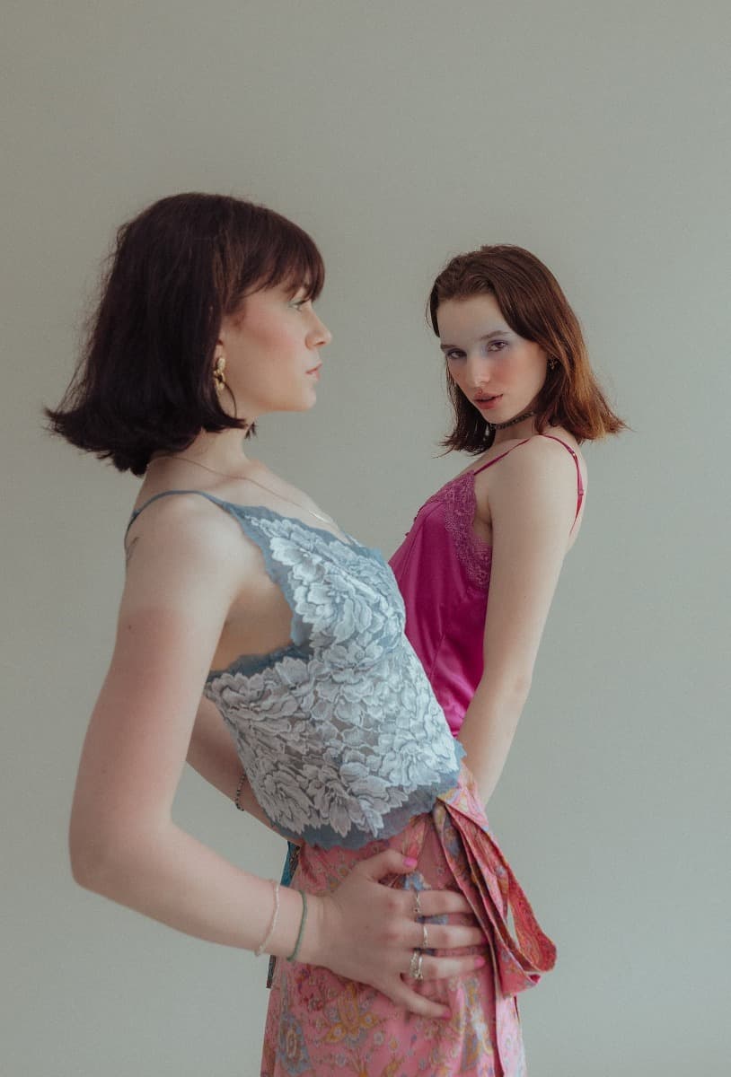 Two models, one in a pink top and the other in a blue lace top, posing together at Revelator Studio in Shreveport, highlighting the ethereal and creative photoshoot at this natural light photography studio.