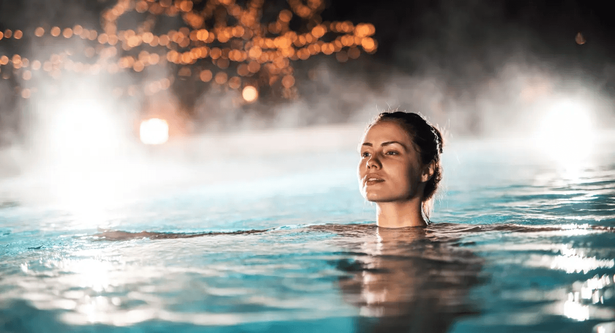 A person partially submerged in a pool, surrounded by mist and soft lighting, creating a serene atmosphere.